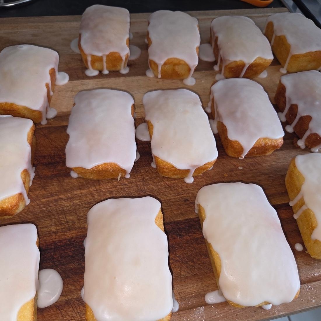Rows of freshly glazed mini drizzle loaves cooling on a wooden board